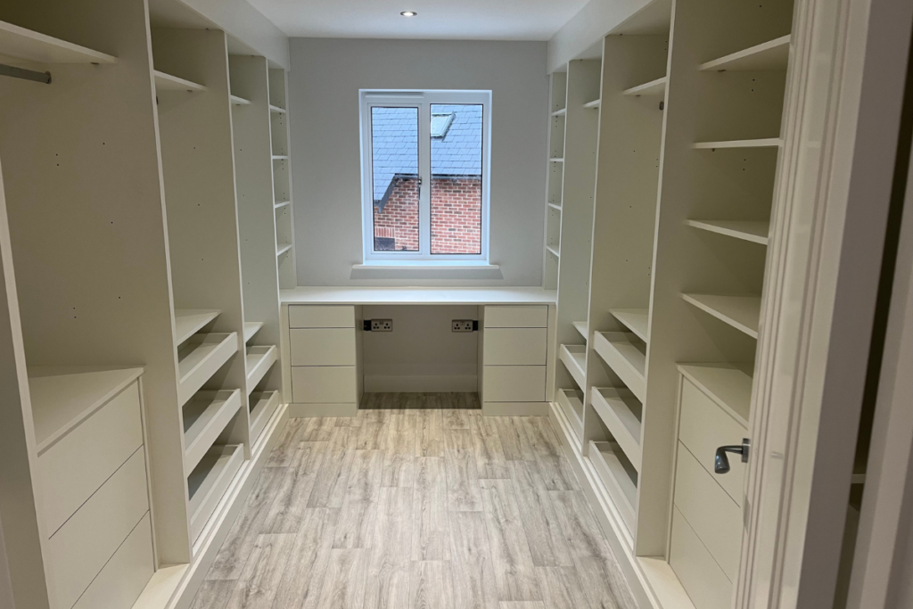 A spacious walk-in closet featuring white cabinets and a stylish desk for organisation and convenience.