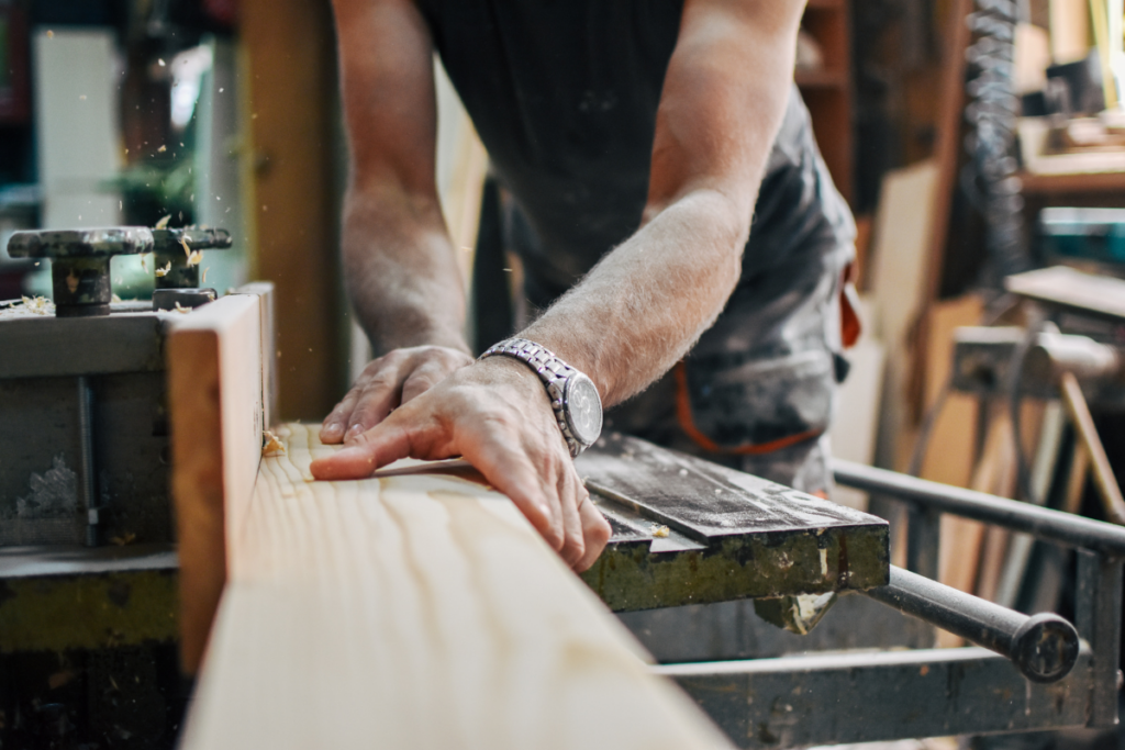 A man diligently shapes a piece of wood, showcasing craftsmanship and focus in his woodworking project.