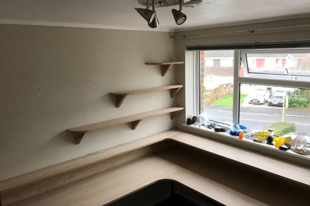 A corner desk with shelves beside a window, creating a bright and organized workspace.