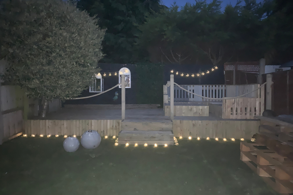 A cozy backyard featuring a wooden deck adorned with string lights, creating a warm and inviting atmosphere.